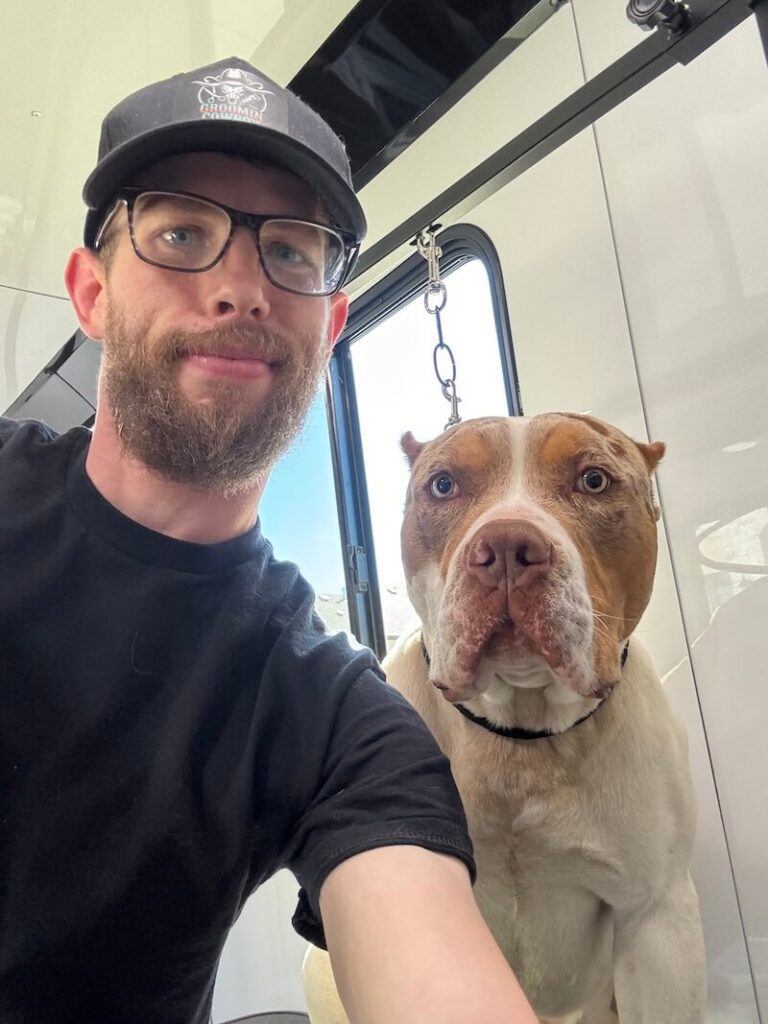 Steven smiling with a happy canine customer at The Groomin' Cowboy Mobile Saloon