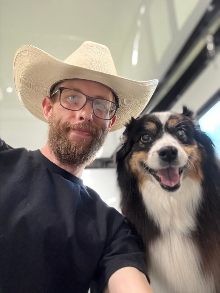 Steven wearing a cowboy hat and posing with a happy canine customer at The Groomin' Cowboy Mobile Saloon