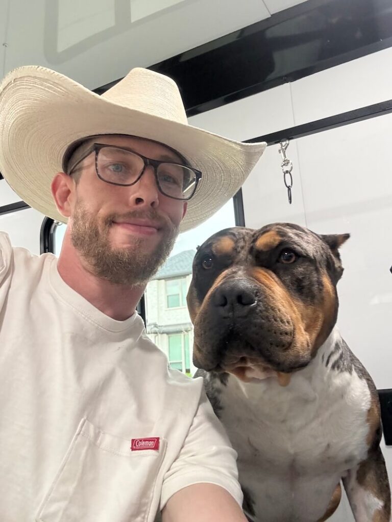 Steven wearing a cowboy hat and posing with a happy canine customer at The Groomin' Cowboy Mobile Saloon