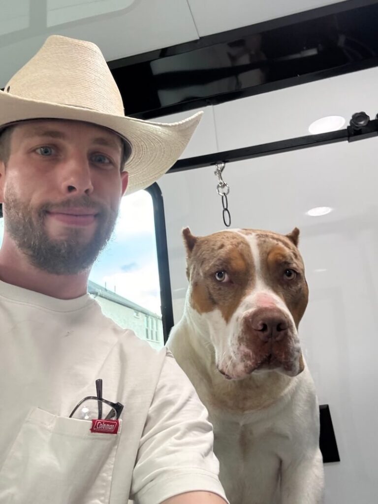 Steven wearing a cowboy hat and posing with a happy canine customer at The Groomin' Cowboy Mobile Saloon